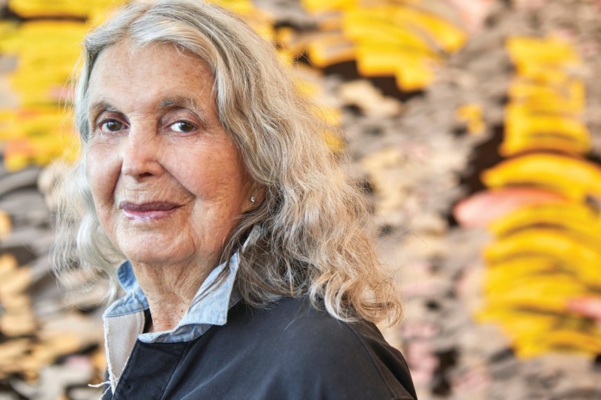 Tight headshot of Judith Murray stading in front of one of her extremely textured paintings.