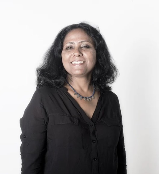 Portrait of artist Tayeba Begum Lipi wearing a black V-neck blouse standing against a white backdrop.