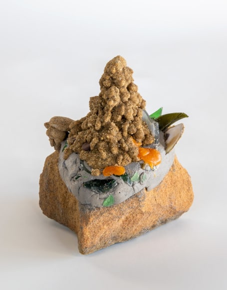 a sculpture by Lily Cox-Richard of a dribbled sand castle on a stone with broken glass shards around its edges