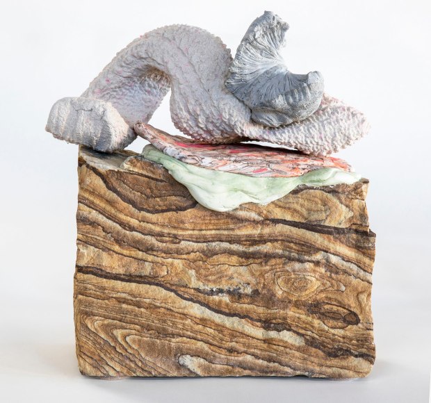 a sculpture by Lily Cox-Richard of plaster casts of tree bark, a sweater sleeve and part of a basket, all stacked on top of a piece of sandstone