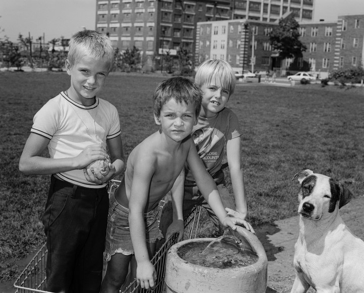 Three kids and a dog by a water fountain in a park. Photograph by Mike Smith