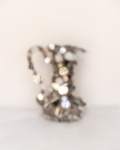 out of focus silver pitcher on a white background, the pitcher has small round mirrors reflecting the landscape behind the camera (in focus)