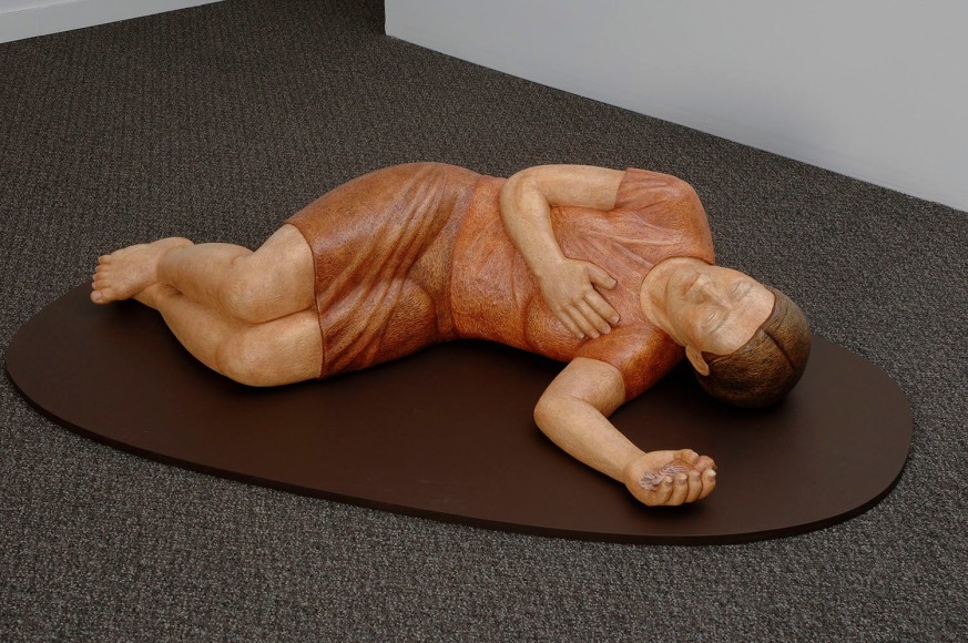 Sachiko Akiyama  I Remember What I Did Not See, 2010  Polychromed Wood  59h x 29w x 15d in. a wood sculpture of a figure lying on the ground in a restful position, with bird in left hand.