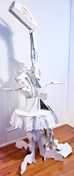 painted paper sculpture of a pitcher pouring over a plant in a planter