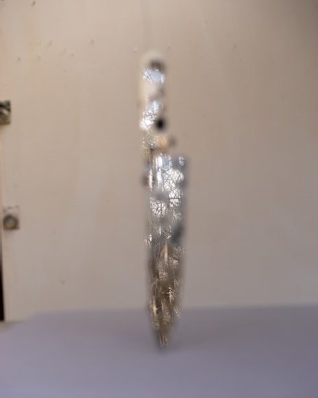 a out of focus knee standing upright on its point on a grey background, the knife has small round mirrors reflecting the landscape behind the camera (in focus)