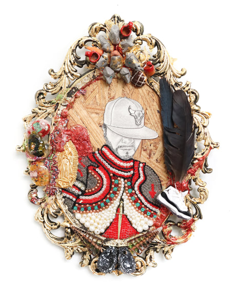 Portrait of a young man in  red robes with a baseball cap pulled down over his eyes. framed in an ornate oval shaped framed with beads, feathers and found objects