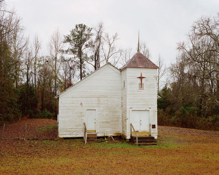 Horizontal photograph of white wooden slat windowless church in the middle of a pasture