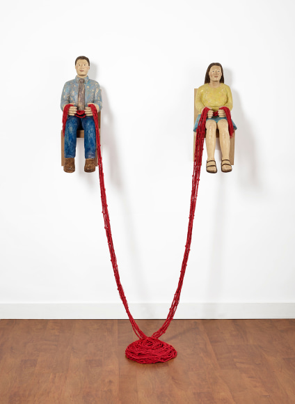 Sachiko Akiyama  Gathering, 2019  Wood, Paint,String  Dimensions Variable. a sculpture of two figures mounted to a wall with a length of red cord connecting them together and to the floor below.