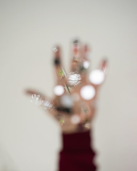 out of focus photograph of a hand with its fingers spread in the center of the image, the hand olds small round mirrors reflecting tree branches behind the camera