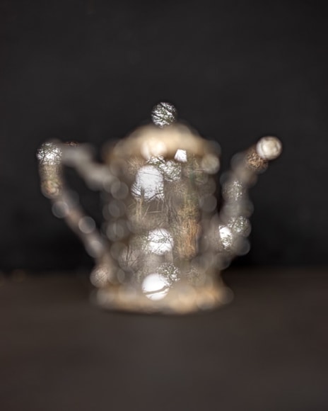 an out of focus silver coffee pot on a black background, round silver mirrors reflect the outside