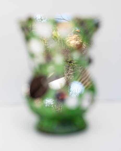 An out of focus green vase on a white background with small mirrors reflecting an in focus landscape
