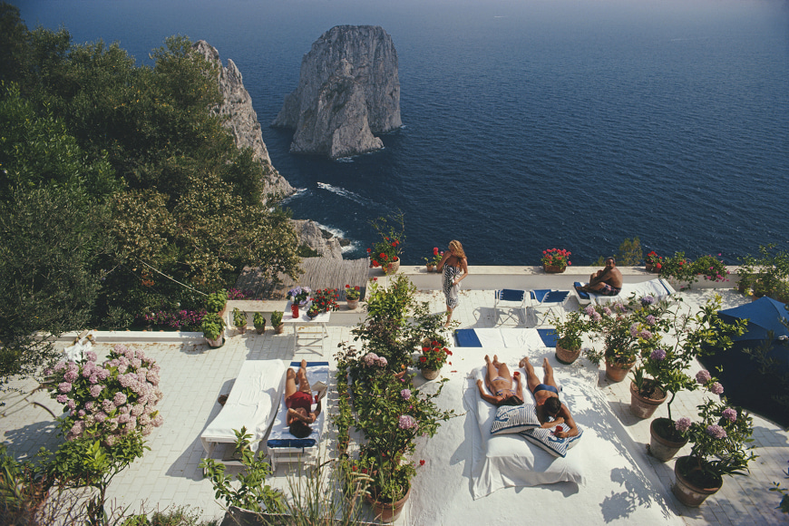 Slim Aarons, Il Canille, 1980: Sunbathers lounge on the terrace of Il Canille, built into the rocks of Pizzolungo overlooking the waters off the coast of Capri, Italy
