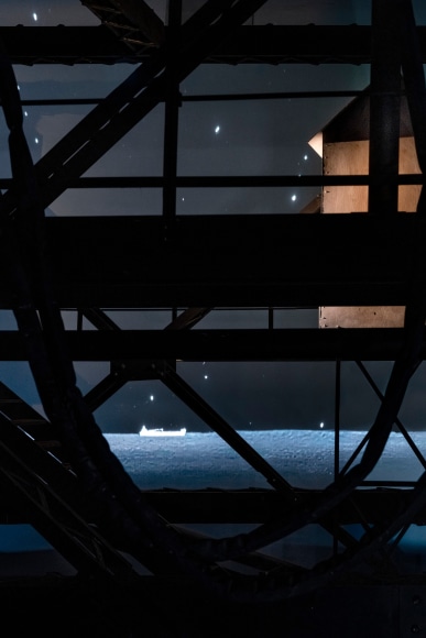 Ship/Dock/Three Houses and the Night Sky, 2023, Wood, plastic, glass, acrylic paint, electrical fixtures, metal, video projections, sound, darkness, 12’ x 29’9” x 14’9”