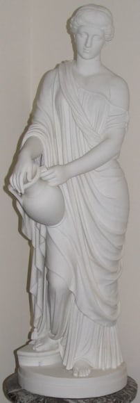 Image of white marble statue titled &quot;Woman of Samaria&quot; by William Rinehart depicting a woman, in a draped garment with many folds, holding a water jug at her hip.