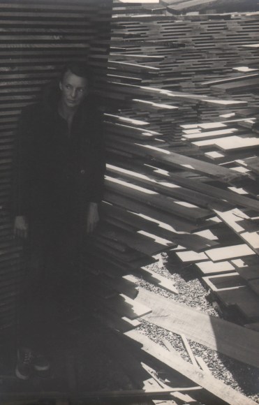 PaJaMa, Margaret French, Provincetown, ​1947. A woman stands in shadow on the left of the frame, surrounded by stacked planks of wood.