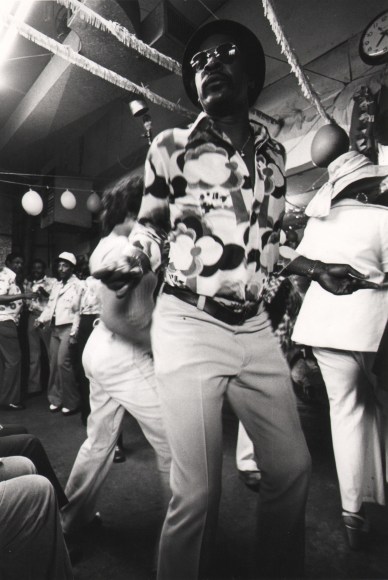 38. Mikki Ferrill, Untitled, c. 1970. A man in sunglasses photographed from a low angle, dancing in a crowded dance hall.
