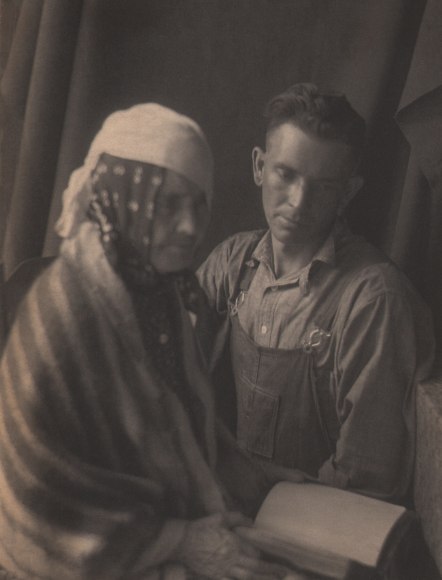Doris Ulmann, Untitled (Soothsayer), ​1928&ndash;1934. Two seated figures, the front-left figure is out of focus and covered in a shawl and headscarves, holding a book. The man on the right looks down at the book.