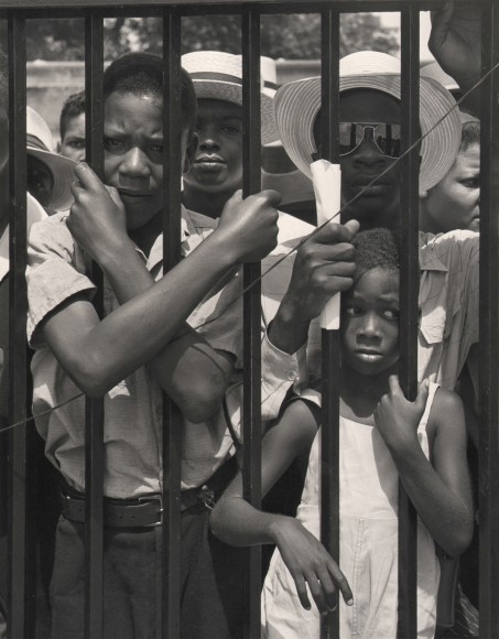 Wayne Miller, Untitled, Chicago, 1946&ndash;1947. A group of men, with one younger boy in front, stands behind the vertical black bars of a fence, looking to the camera.