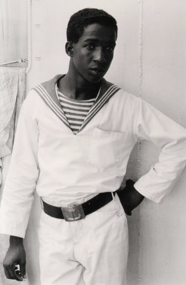25. Shawn Walker, Untitled, ​c. 1970. A man stands in a white sailor's uniform with one hand at his hip.