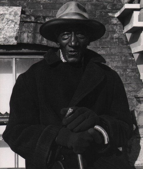 Marvin E. Newman, Chicago, ​1950. An older man in a hat, coat, and gloves holds a cane and a cigar, looking into the camera.