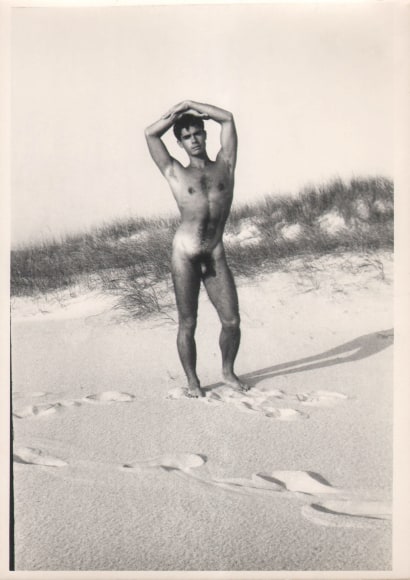 PaJaMa (Jared French), Jos&eacute; Martinez, Fire Island, ​c. 1945. Nude male stands in the midground on the beach, looking to the camera with hands resting atop his head.