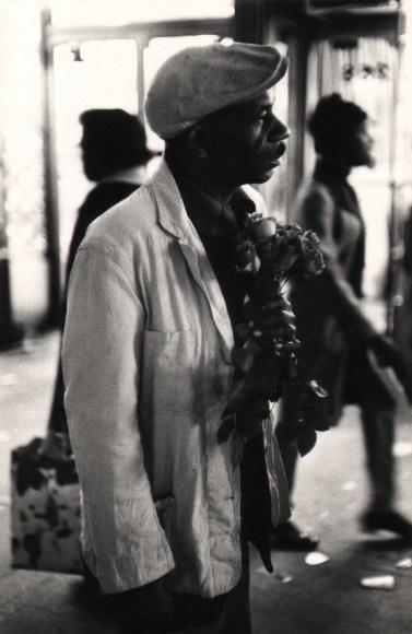 02. Beuford Smith, Man with Roses, 125th Street, ​1972. Upper body portrait of a man facing the left of the frame holding a small bouquet of roses.