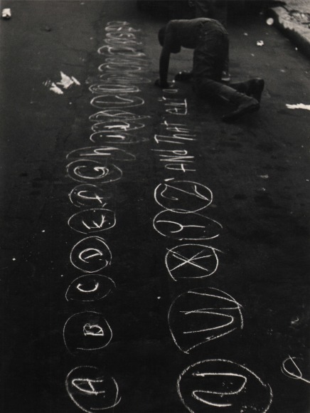 17. Beuford Smith, Brooklyn, NY, ​c. 1970. A young boy crouches on the street with chalk, writing the alphabet with each letter in a circle.