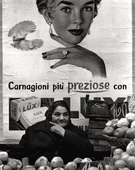 Nino Migliori, Northern People, 1953. A middle-aged fruit vendor poses similarly to the woman in the advertising illustration behind her.