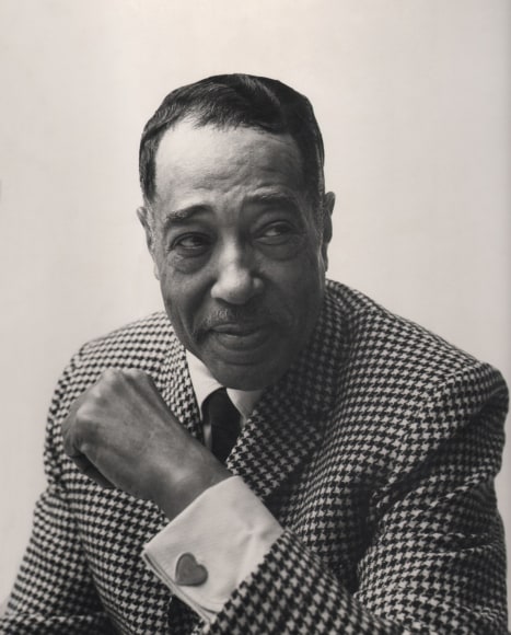 Chuck Stewart, Duke Ellington, ​1955. Subject smiles with eyes cast to the right, with one arm raised in front of his chest to reveal a heart-shaped cufflink.