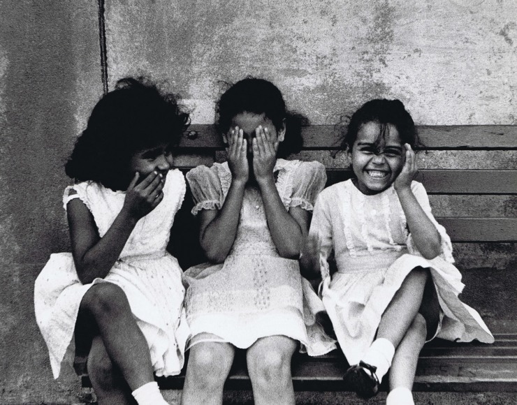35. Beuford Smith, Three Girls, Bronx, 1968. Three girls in white dresses seated on a bench. From left to right, one has a hand to her mouth, the next has hands covering her eyes, the last has one hand covering an ear.