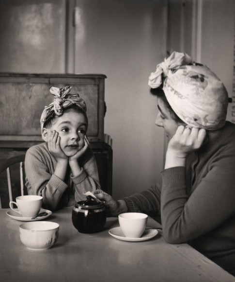 34. M. Gray, A perfect mother and daughter picture, with the child subconsciously mimicking the mannerisms of her mother, 1961. A little girl and mother look at each other with heads resting in their hands and matching headwraps as they sit at a table set for tea.
