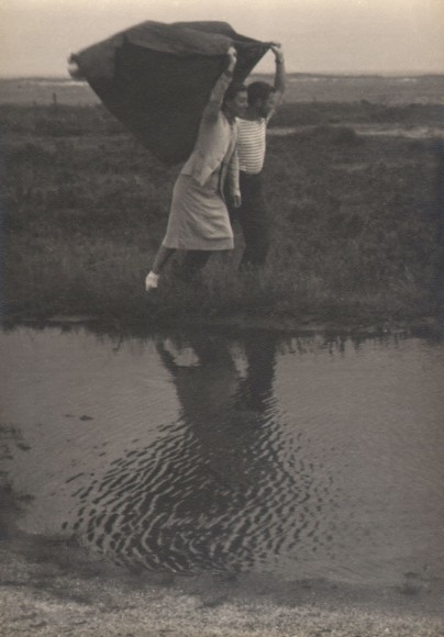 PaJaMa, Fidelma Cadmus &amp; George Tooker, Nantucket, ​c. 1945. A man and woman walk through a grassy area holding a cloth above their heads, which blows back towards the left in the wind. A pool of water is between the figures and the camera.