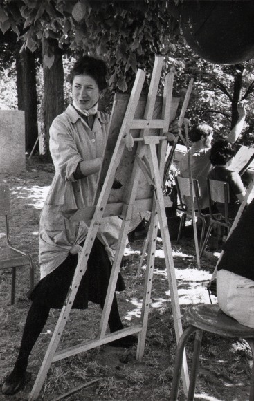 51. Janine Ni&eacute;pce, Jeunes filles de Paris, c. 1960. A woman stands outdoors at an easel wearing a smock and smiling towards the left of the frame.