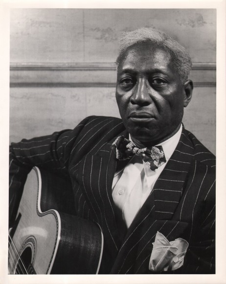 Gordon Coster, Leadbelly, ​c. 1940. Subject holds a guitar and looks into the camera with a serious expression.