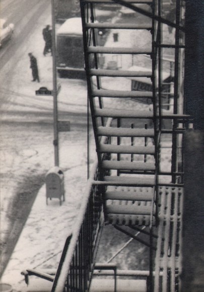 42. W. Eugene Smith, As From My Window I Sometimes Glance, ​1957&ndash;1958. Elevated view of a snowy fire escape. Two figures, a mailbox, and cars can be seen on the street below.