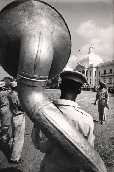 02. Graham Finlayson, Haiti - Presidential band before the Palace, c. 1958&ndash;1966. Rear view of a uniformed man with a large wind instrument strapped to his back.