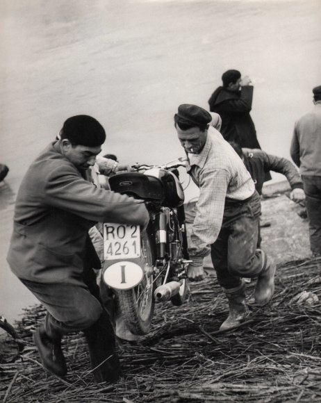 Pietro Donzelli, Flood in Polesine, ​1960. Two men carry a motorcycle uphill towards the camera.