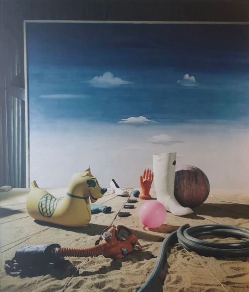 Hi Williams, Rubber Dal&iacute;, ​1941. Composition of various rubber objects on sand with a blue sky and clouds painted background.