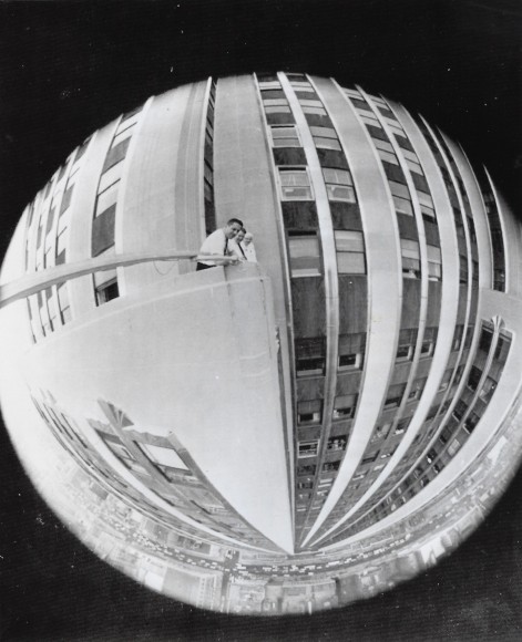 06. New York Journal, A Nice Round Figure, ​1962. Fish-eye lens view of three figures on a balcony of the Empire State Building. The image is distorted so that the view is a circle.