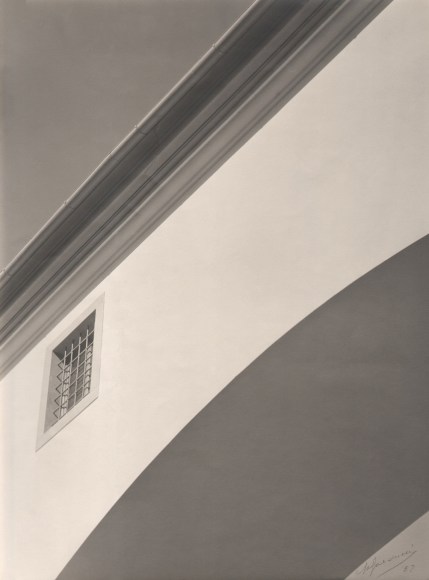 Alberto Galducci, Architettura, c. 1952. Detail of a building with a barred window in the lower left of the frame. Diagonal, geometric composition with dramatic light and shadow.