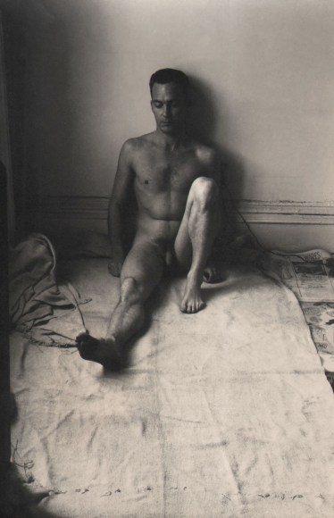 PaJaMa, Bob Wallace, ​1947. Male nude, eyes closed, facing the camera, seated against an indoor wall, one leg bent and the other extended outward.