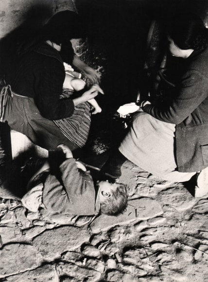Federico Patellani, Fede e magia nell'Italia del Sud, ​c. 1955. Two woman kneel on stone ground. A young boy lays beside them and an infant is in the lap of the woman on the left.