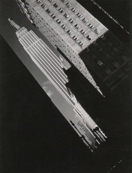 26. John C. Hatlem, Empire State Building, ​c. 1935. Street view tilted diagonally left showing the Empire State Building between other buildings cast in dark shadows.