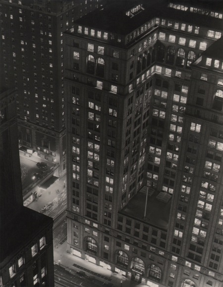 Paul J. Woolf, Grand Central, ​c. 1935. Night time view looking down towards two intersecting streets and tall buildings rising above them.