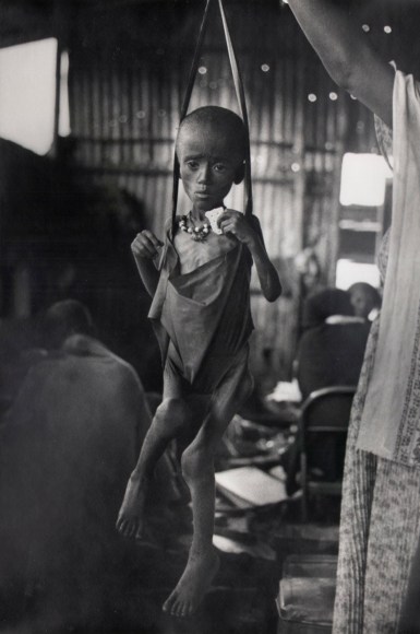 19. Ethiopian Girl Clutches Biscuit: an Ethiopian girl clutches a biscuit as she is weighed in a tent where a medical team from Doctors Without Borders were providing care, 1984.