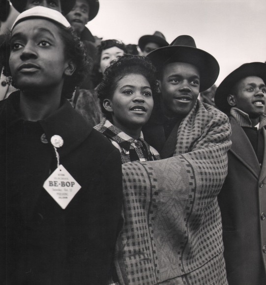 Wayne Miller, High School Football Game, Chicago, ​1946&ndash;1947. A large group of teenagers. A couple embraces with a blanket wrapped around them. Another teen in the foreground wears a &quot;Be-Bop&quot; pin.