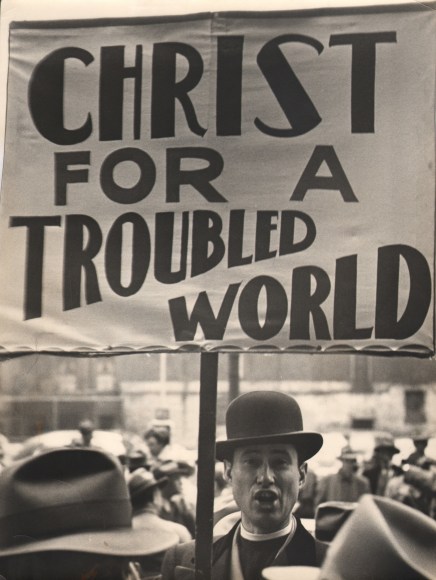 25. Simpson Kalisher, Untitled, ​1949. A man in a bowler had holds a large sign above his head that reads &quot;Christ for a troubled world&quot;.