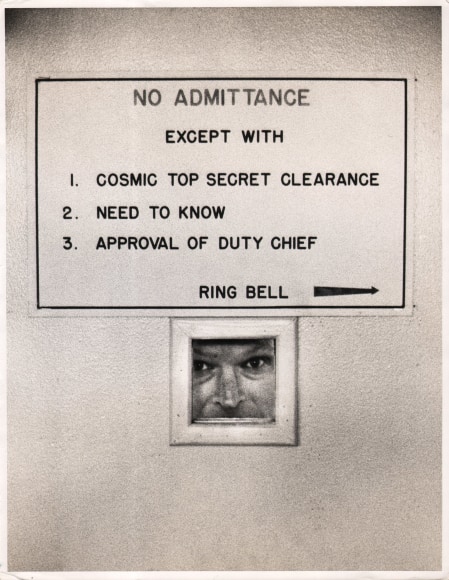 52. Howard Sochurek, General Norstad, NATO Paris, ​1958. A man looks through a small opening in a door marked &quot;No admittance except with 1. Cosmic top secret clearance, 2. Need to know, 3. Approval of duty chief. Ring bell&quot;