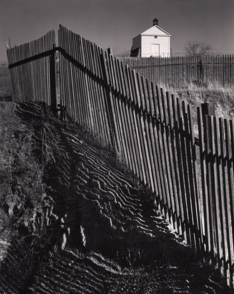 Ansel Adams, The White Church, Hornitos, California, ​1946. Frame is divided from lower right to upper left by a wooden fence. A small white building occupies the upper right.