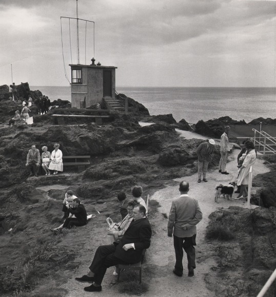 14. C. O'Gorman, A holiday scene at North Berwick with everybody doing something as though compelled by the traditions of seaside behaviourism, 1963. Seaside pathway with scattered figures sitting and standing. A flagpole and small structure stand in the midground left.